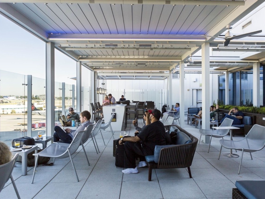 People sit at an airport under an aluminum pergola