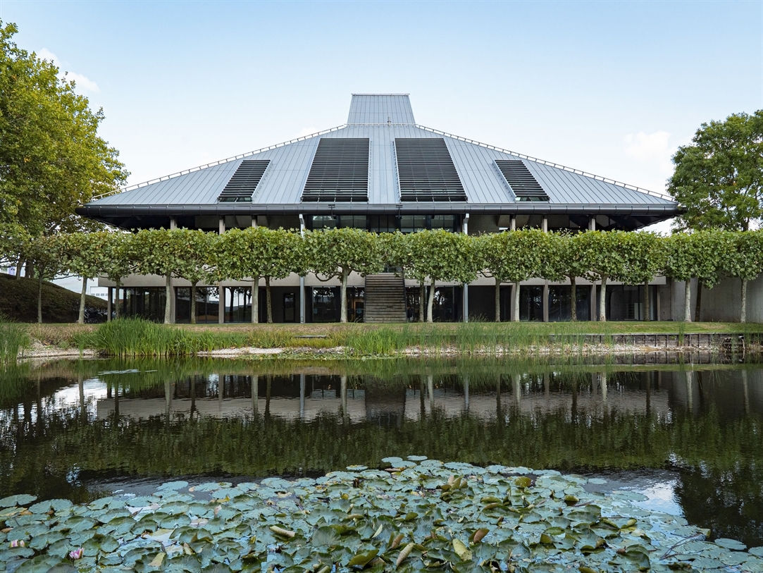 A pond sits in the foreground with a modern buildi