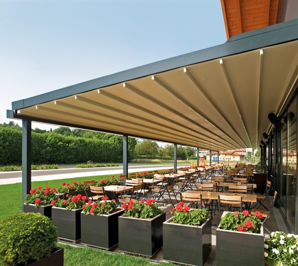 A very large restaurant patio covered by a wall mounted retractable pergola with cream fabric