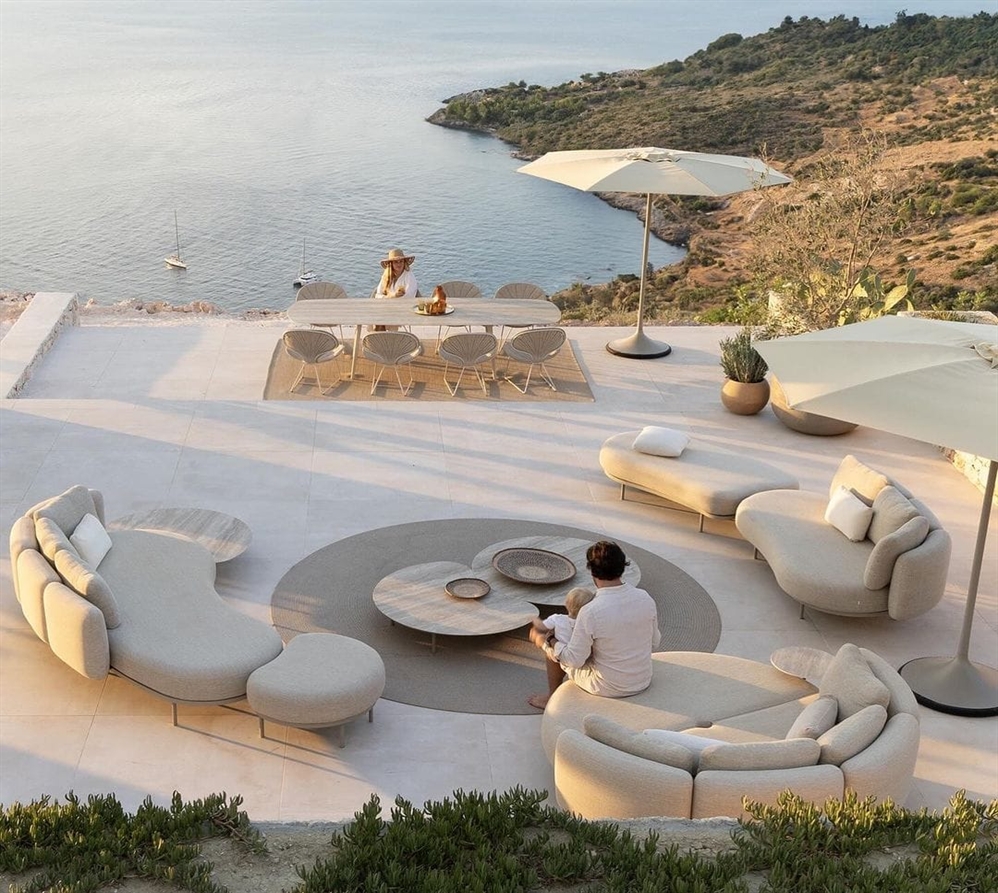 Clifftop terrace with curved modular sofas, dining setup, and ocean view at sunset.